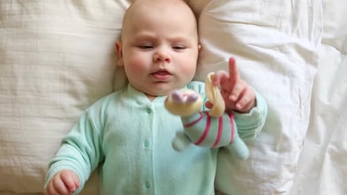 Cute Newborn Baby Lying on the Back and Plays with Colorful Toys