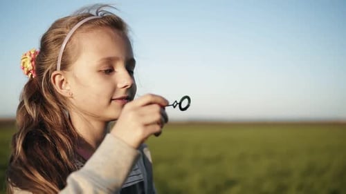 Cute Little Girl is Blowing Soap Bubbles in the Meadow on a Sunny Day