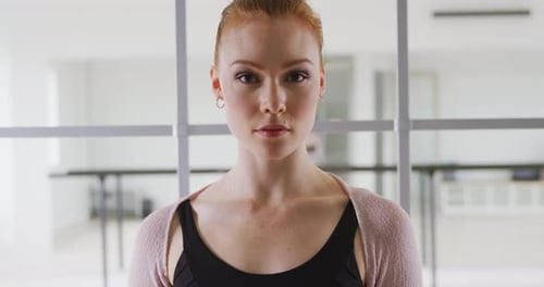 Bailarina de ballet caucásica de pie en un luminoso estudio y mirando a la cámara