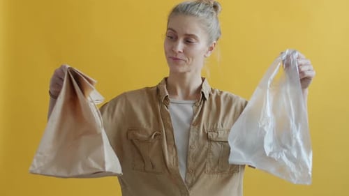 Retrato de una joven que elige una bolsa de papel sobre una de plástico mostrando los pulgares hacia arriba y sonriendo