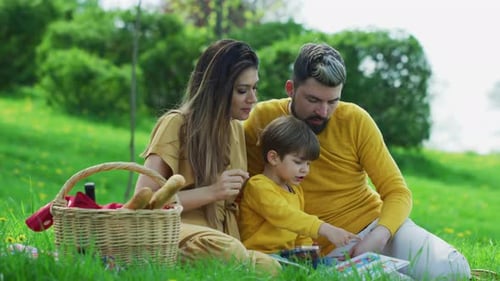 Family Reading Book During Green Meadow Picnic