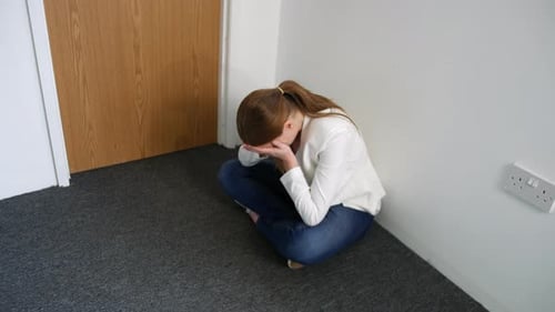 Upset Woman Sitting in Corner With Head in Hands