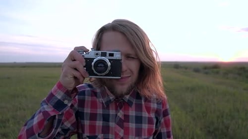 Young Adult Holds Retro Camera in Grassy Field