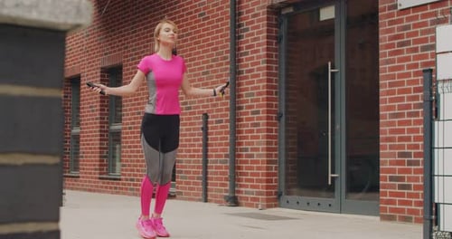 Young Sports Girl is Jumping with a Skipping Rope Outdoors in the City