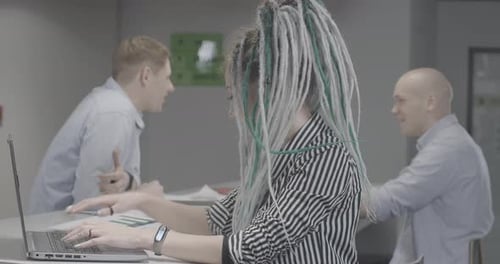 Vue latérale d'une femme concentrée de la génération Y avec des dreadlocks tapant sur un clavier d'ordinateur portable au bureau avec