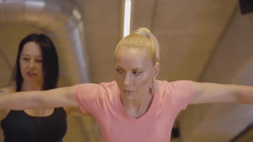 Kamera zoomt aus ernsthafter Sportlerin, die Hanteln hebt, mit Personal Trainer, der sie anpasst