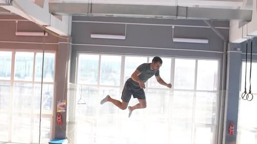 Young Fit Happy Man Jumping and Flying on Trampoline in Fitness Gym