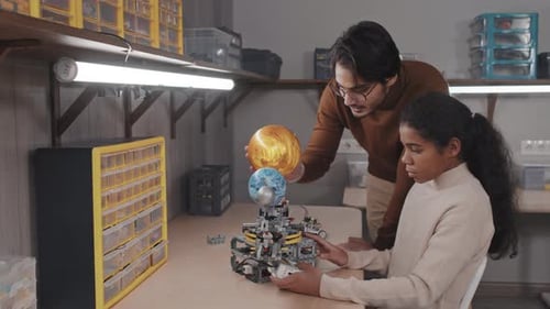 Teacher Helping Girl With Robotic Solar System Model