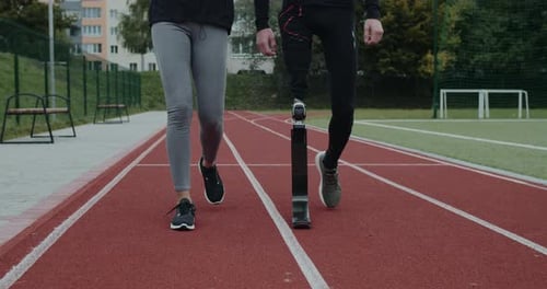 Crop View of Unknown Woman and Disabled Man with Prosthetic Leg Walking at Sports Field