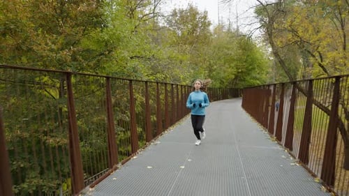 Female Jogger with Headphones Running on Bridge in Park