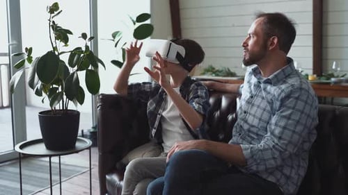 Boy Enjoys Virtual Reality Game Beside Adult on Couch