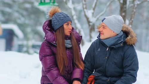 Girl and Boyfriend in Jackets Talk Sitting in Snowy Park