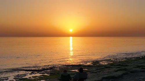 People sit on the beach and watch the sunset
