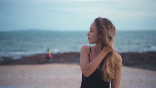 Portrait of a blonde caucasian woman on a beach touching her hair on windy day. Pretty blonde female