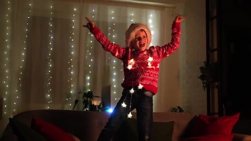 Excited Christmas Boy Dancing in Santa Hat at Home Evening