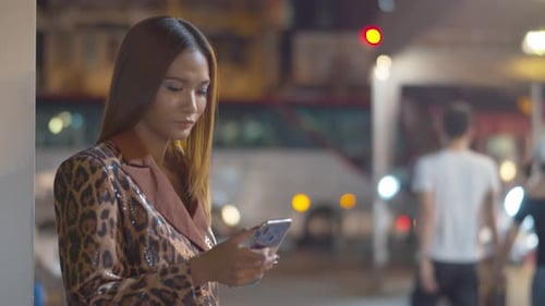 Superbe jeune femme vérifie son smartphone pour les messages et les médias sociaux sous la rue lumineuse de la ville