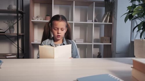 Girl Reading a Book Indoors at a Table