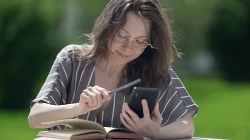 Woman Using Smartphone and Writing Outdoors in Park