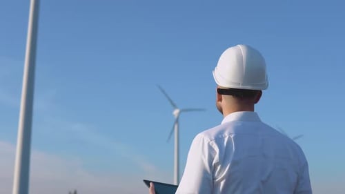 A Male Engineer in a White Helmet and a Classic Shirt Inspects the Power Plant's Capacity with a