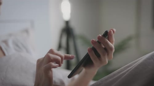 Unrecognizable Woman Uses Smartphone While Lying in Bedroom