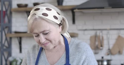 Close-up Face of Beautiful Senior Caucasian Woman Cooking Indoors. Cheerful Brown-eyed Female