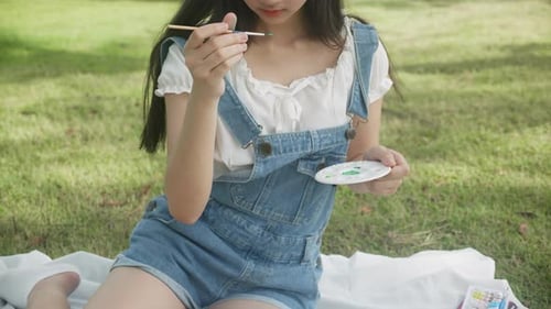 Young asian woman sitting drawing picture with colorful paint brush while leisure in the park.