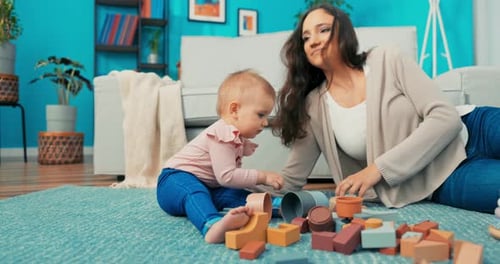 Girl is Sitting on Carpet with Mother Putting Together Tower of Blocks Daughter is Destroying