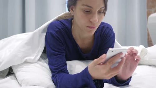 Woman Using Phone Lying in Bed Indoors