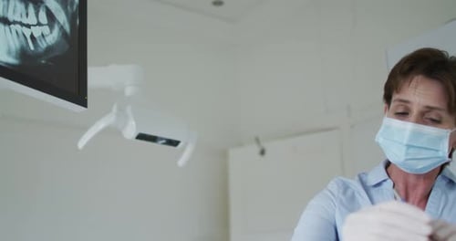 Caucasian female dental nurse with face mask examining teeth male patient at modern dental clinic