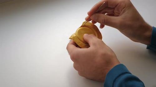 Homem com as mãos trêmulas coça doce de açúcar mascavo e caramelo com agulha de metal.