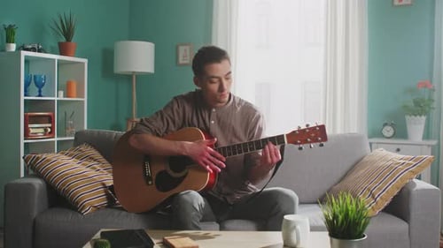 Young Adult Plays Acoustic Guitar on Couch