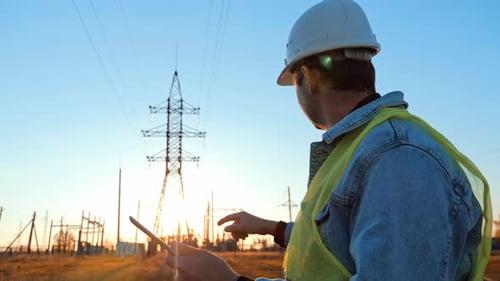 Silhouette of Engineer Walk on Field with Electricity Towers