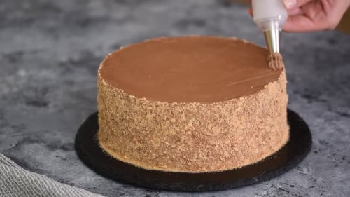 Frau, die Kuchen mit Schokoladencreme dekoriert, hält Spritzbeutel in der Küche