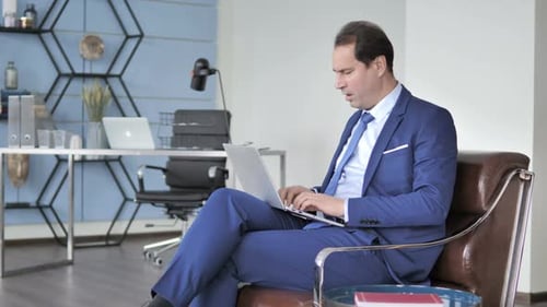 Man in Suit Working on Laptop, Coughing