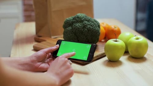 Closeup of Woman's Hand Browsing Smartphone with Chroma Key on Kitchen at Home.