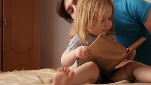 Man Reads Book with Child on Bed