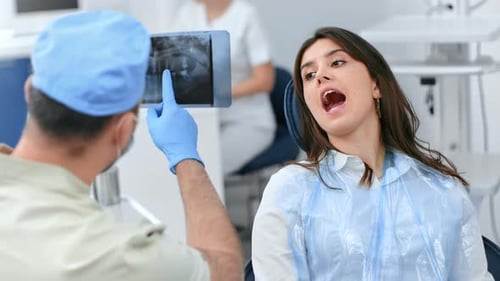 Male Dentist Pointing on x Ray Image Consulting Female Patient Open Mouth on Chair at Stomatology