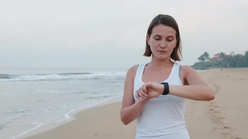 Woman Checking Watch Then Jogging on Sandy Beach