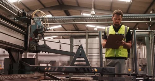 Man Inspecting Industrial Machine with Clipboard in Factory