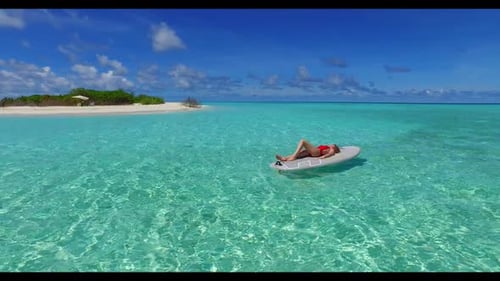 Man and woman sunbathing on tropical seashore beach vacation by aqua blue lagoon with white sandy ba
