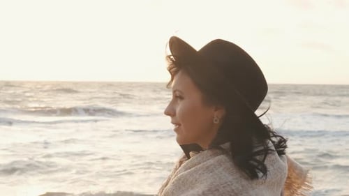 Portrait of Romantic Brunette Woman in Hat and Coat Walking on the Beach in Autumn at Sunset or
