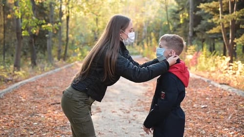 Woman Adjusts Mask on Child in Autumn Park