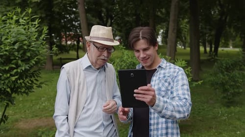 Grandfather and Grandson Using Tablet in Park