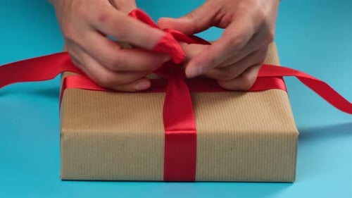 Hands Tying a Red Ribbon on a Gift