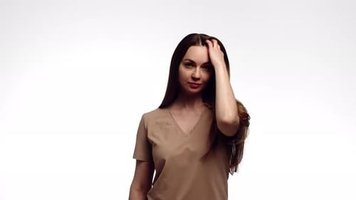 Attractive Woman Runs Hand Through Long Brown Hair Stands on White Background in Studio Front View