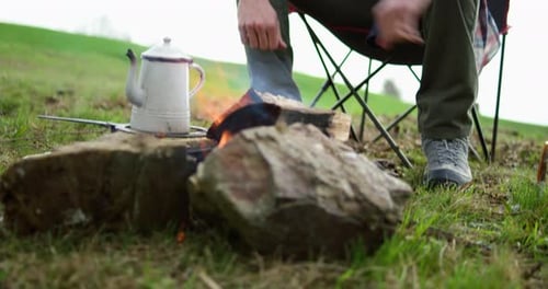 Camper Whittling Sticks near Campfire with Kettle