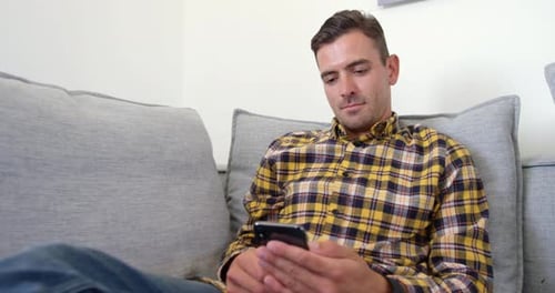 Man Relaxing on Couch Using Mobile Phone