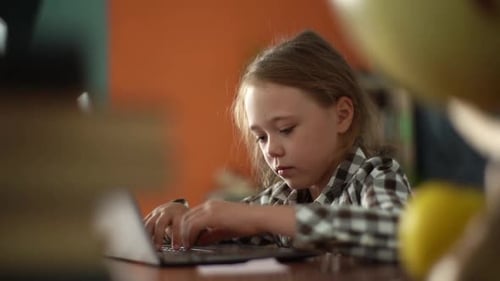 Closeup Side View of Adorable Primary Child Girl Using Typing on Keyboard of Laptop Sitting at Desk