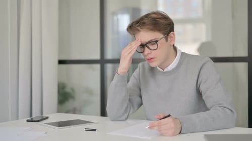 Young Man Reacting to Loss While Writing on Paper in Office