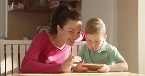Woman and Boy Using Smartphone at Table